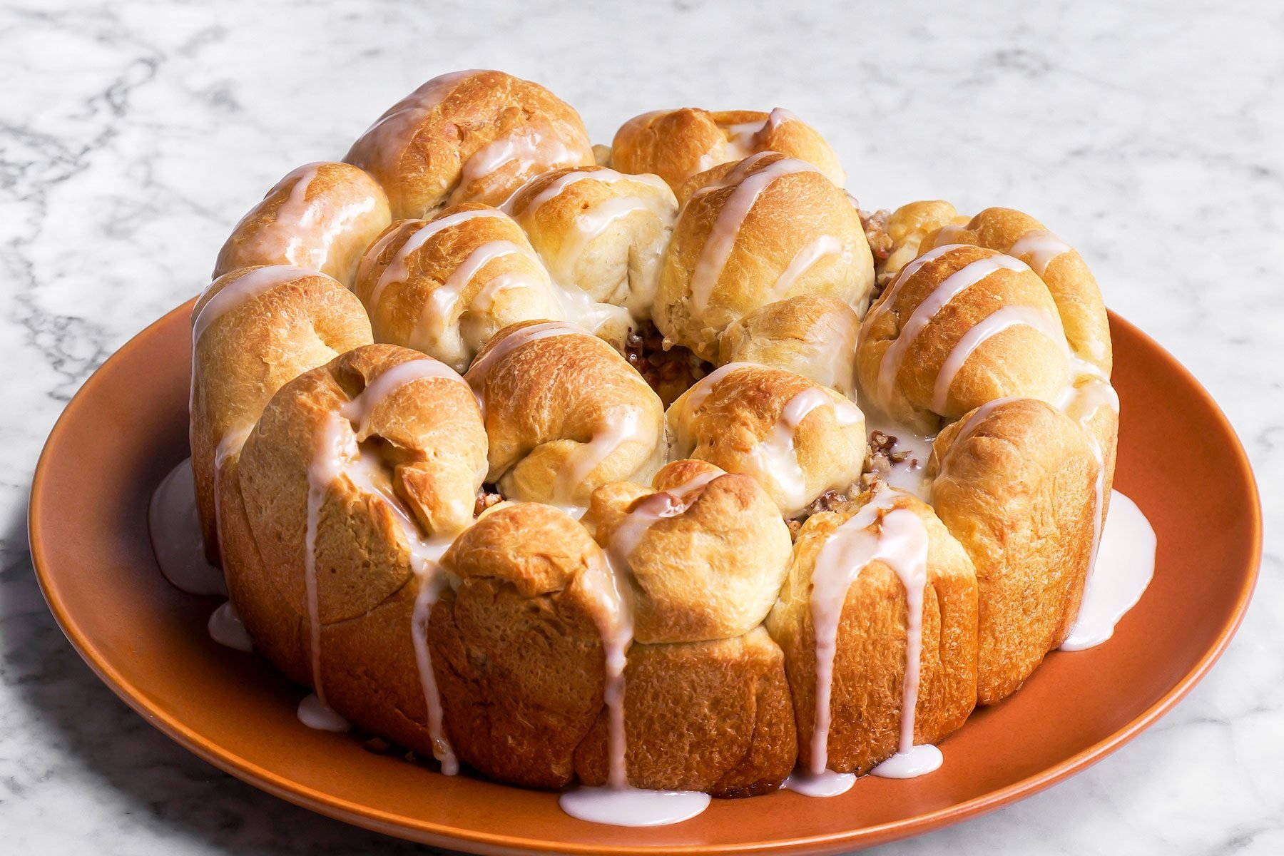 Apple Monkey Bread drizzled with icing and kept on a rust plate on a counter.