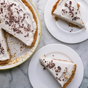Overhead shot of Banoffee Pie in a large pie plate; sliced and served on two plates; with a fork resting on a light green napkin; all set on a marble-textured surface