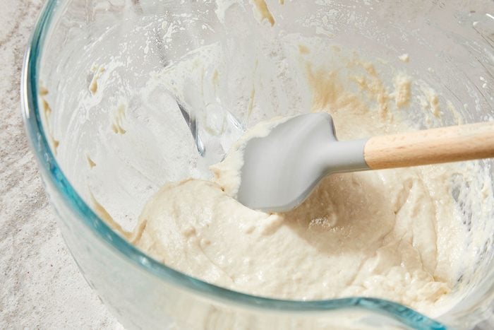 Overhead shot of a glass bowl filled with thick, creamy batter; with a silicone spatula resting inside; streaks of batter cling to the sides of the bowl; set on a light-colored surface. 