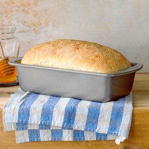 Baked bread loaf in a loaf pan laced on a table with a clothe underneat it